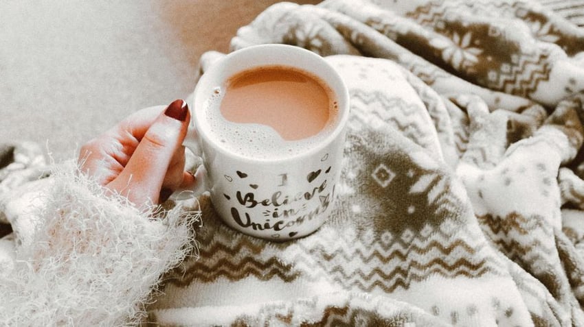 Woman having a cup of tea while wrapped in a winter blanket