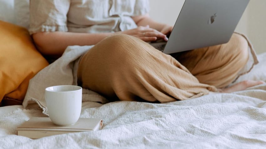 Women sitting in bed working on a laptop with a cup of tea and a book